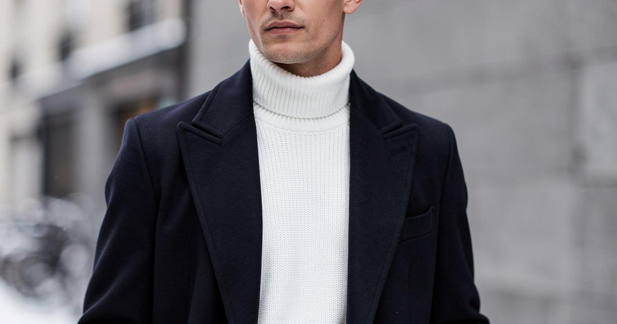 Homme portant un pull blanc à col roulé sous un manteau marine en hiver